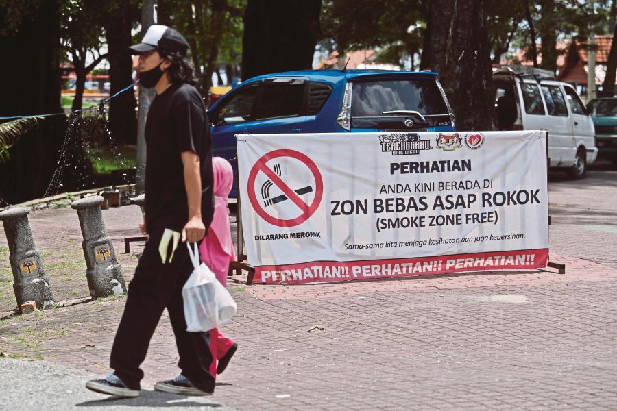  A parent walking his child  past a sign proclaiming that  a public beach in Kuala Terengganu  is a smoking-free zone. -NSTP/GHAZALI KORI   