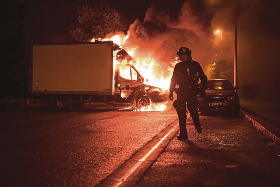 An anti-riot policeman walking past a burning truck in Nantes, western France, early yesterday. AFP PIC 