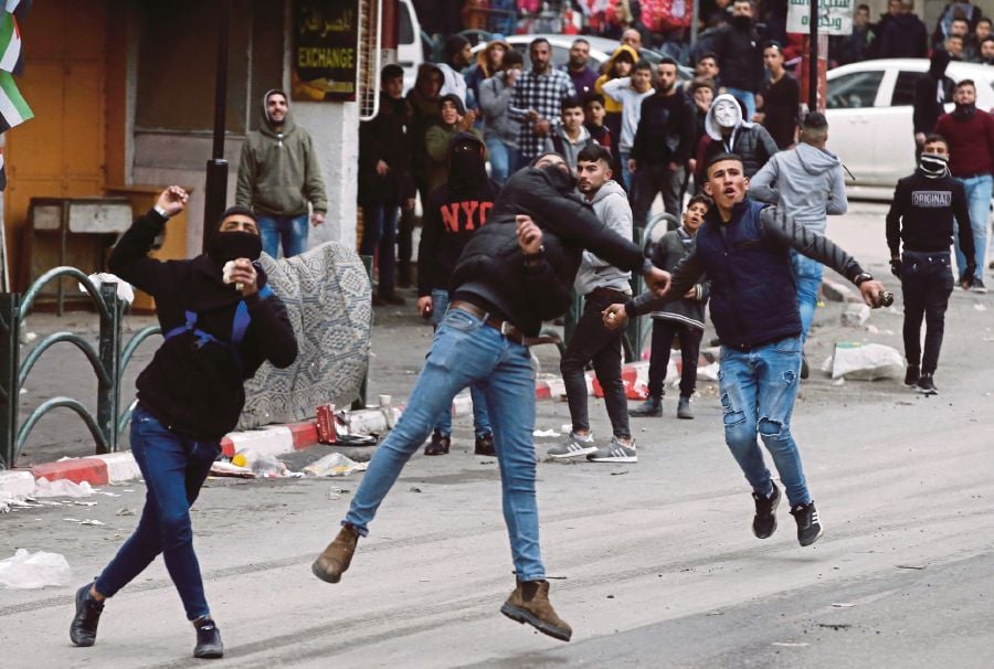 Palestinians hurling stones toward Israeli troops during clashes with them at a protest against the US-brokered proposal for a settlement of the Middle East conflict, in the Israeli-occupied West Bank city of Hebron on Sunday. -- Pix: AFP