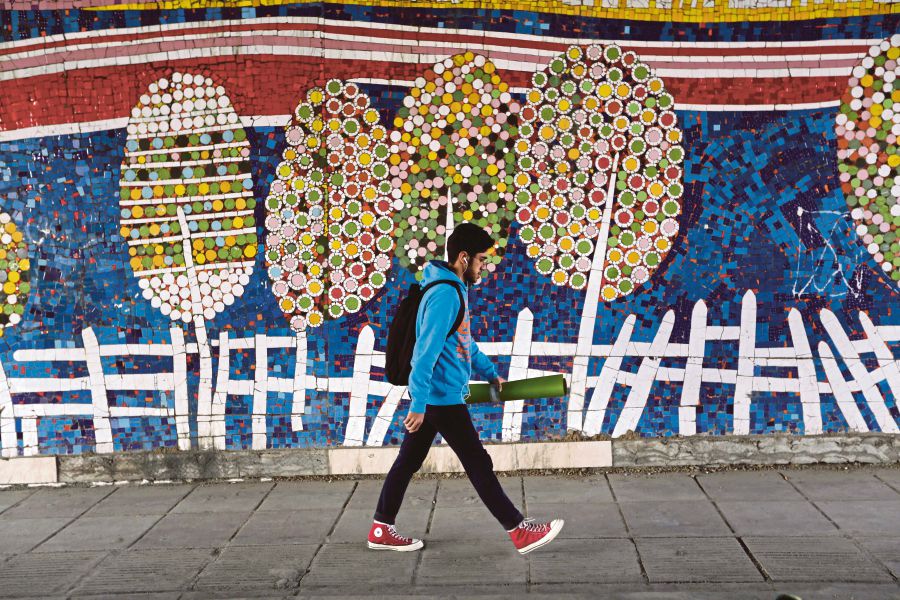 An Iranian man walks past a mosaic-decorated wall in Teheran. Since 1979, the lot of ordinary Iranians has been bad because of economic mismanagement. AFP PIC 