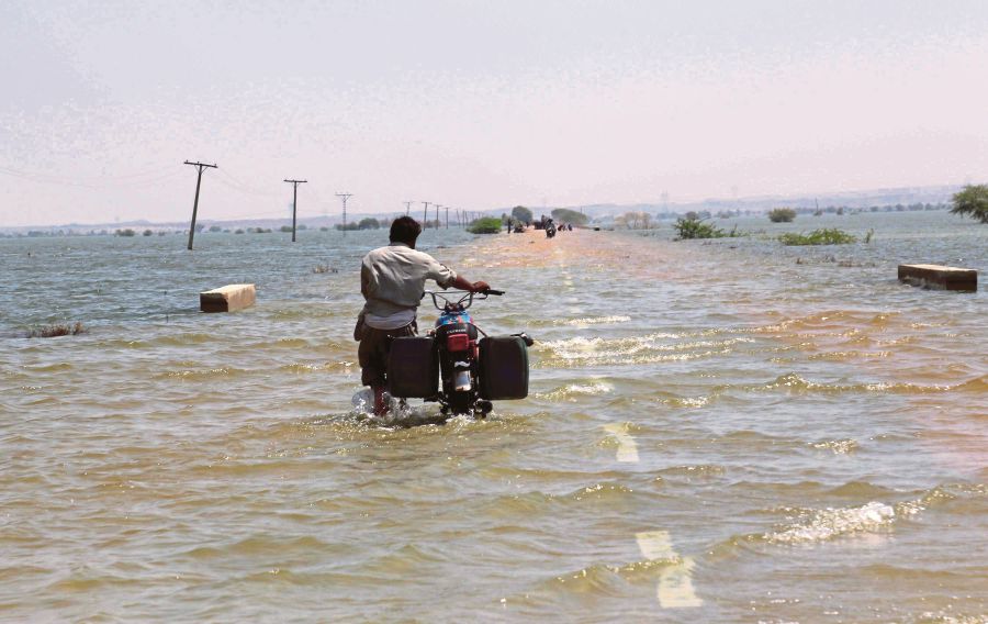A man wading in floodwaters to move his motorcycle to higher ground in Bajara Sehwan, Sindh province, Pakistan, on Friday. Climate change is having catastrophic effects on food security. -EPA PIC
