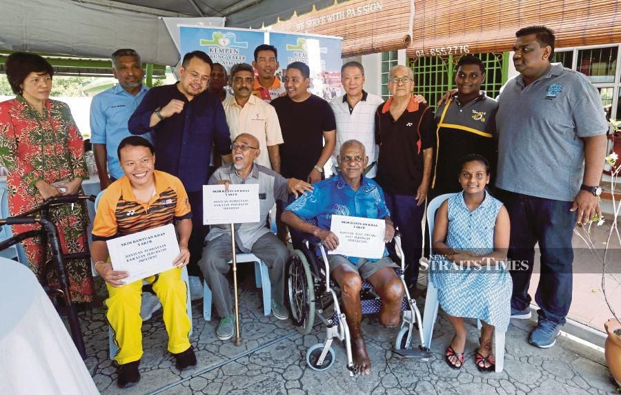 Deputy Youth and Sports Minister Steven Sim (third from left) with aid recipients (seated, from left) Koh Lee Peng, Rahim Mohamad and V. Krishnasamy in George Town yesterday. PIC BY RAMDZAN MASIAM. 