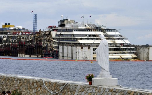 A statue of the Madonna stands at the port of the Tuscan island of Giglio, Italy, as operations to refloat and tow away the luxury cruise ship Costa Concordia get underway, Monday, July 14, 2014. The heavily listing ship was dragged upright in a daring maneuver last September, and then crews fastened huge tanks to its flanks to float it. Towing is set to begin July 21. It's about 200 nautical miles (320 kilometers) to Genoa's port and the trip is expected to take five days. 30 months ago it struck a reef and capsized, killing 32 people. (AP Photo/Giacomo Aprili)Giacomo Aprili