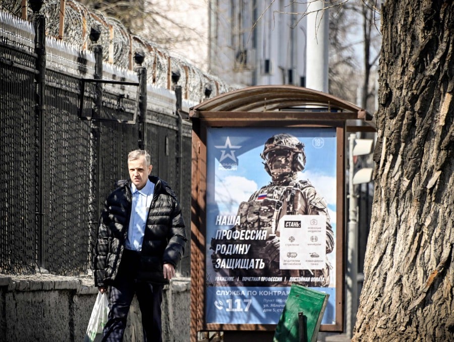 A man walks past a social advertisement billboard showing a Russian soldier and saying "Our Profession - to Defend Motherland" next to the Lefortovo prison, where Evan Gershkovich, US journalist arrested on espionage charges, is held in Moscow on April 12, 2023. -AFP PIC