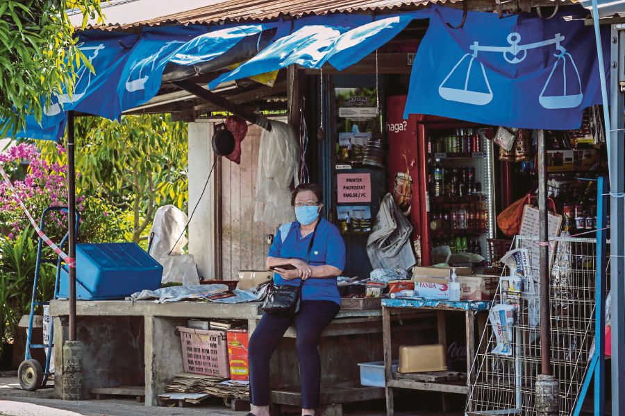 A woman sitting in a shop decorated with Barisan Nasional banners in Tanjung Kling yesterday. Campaigning in the Melaka election has been conducted under strict standard operating procedures. -NSTP/ASYRAF HAMZAH