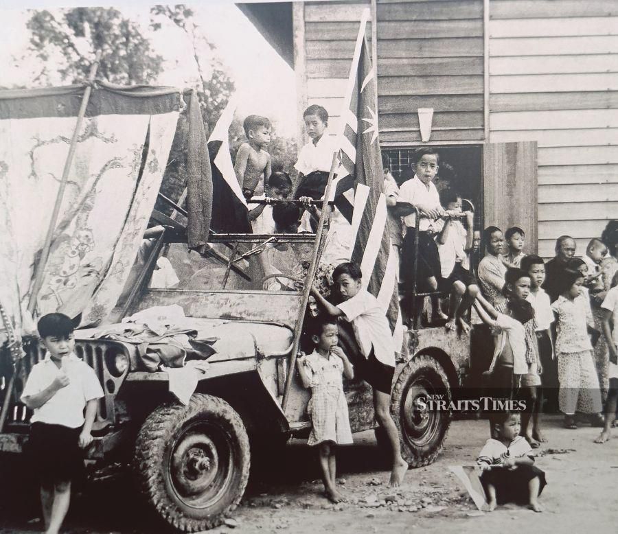 Children clambering onto a military truck with the Malayan flag after Tras villagers were finally allowed to return home seven years following the assassination of Sir Henry Gurney in 1951. - Pic by Alan Teh Leam Seng