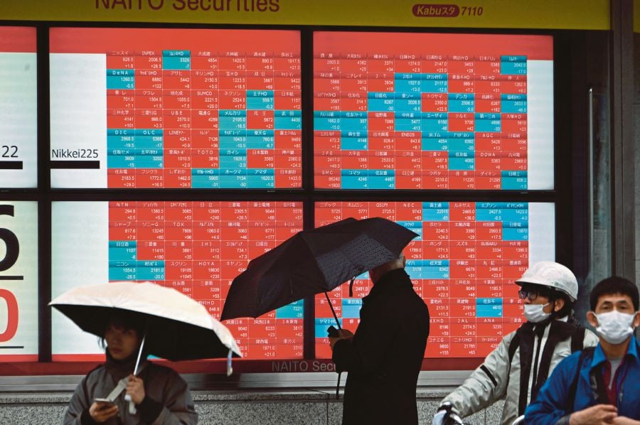Pedestrians stand in front of an electronic board displaying stock prices of each company listed. (Photo by Kazuhiro NOGI / AFP)