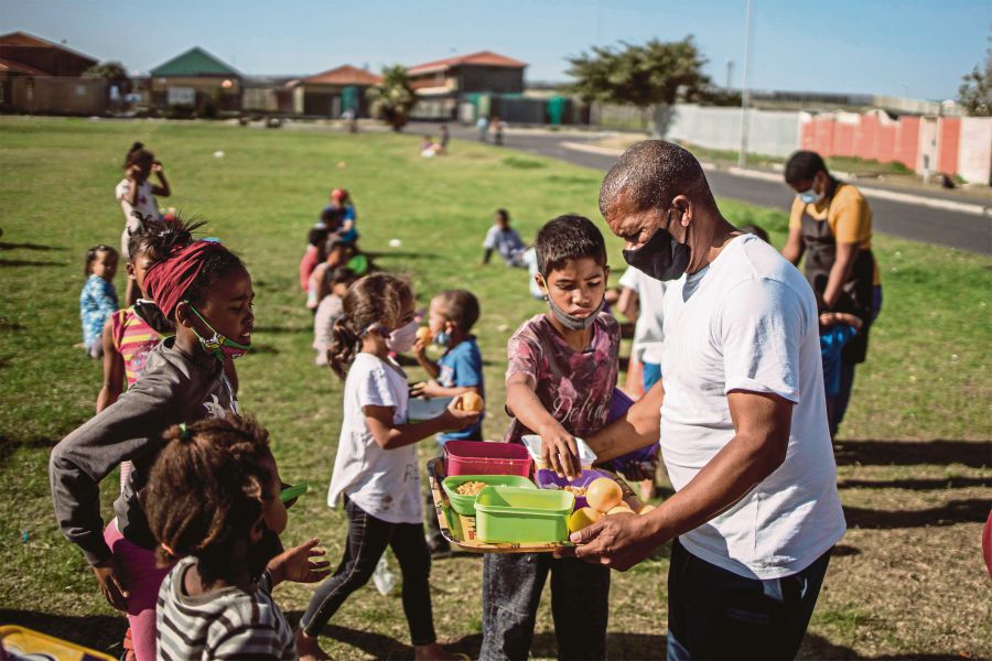 A man (right) distributing food to children in Lavender Hill, Cape Town, recently. AFP PIC