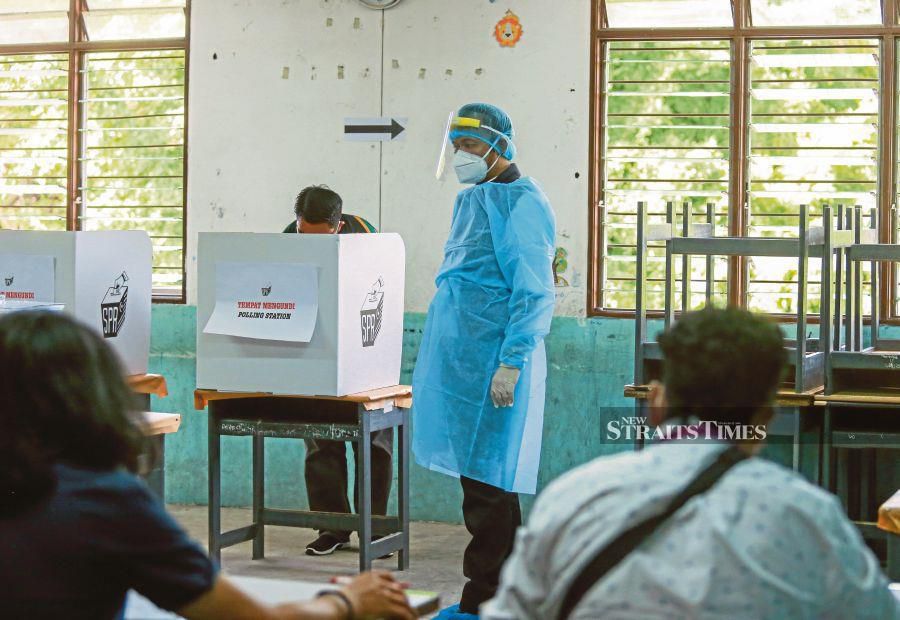A Health Ministry official in personal protective equipment observing voters to ensure physical distancing at SK Sembulan in Kota Kinabalu on Sept 26 last year. - File pic