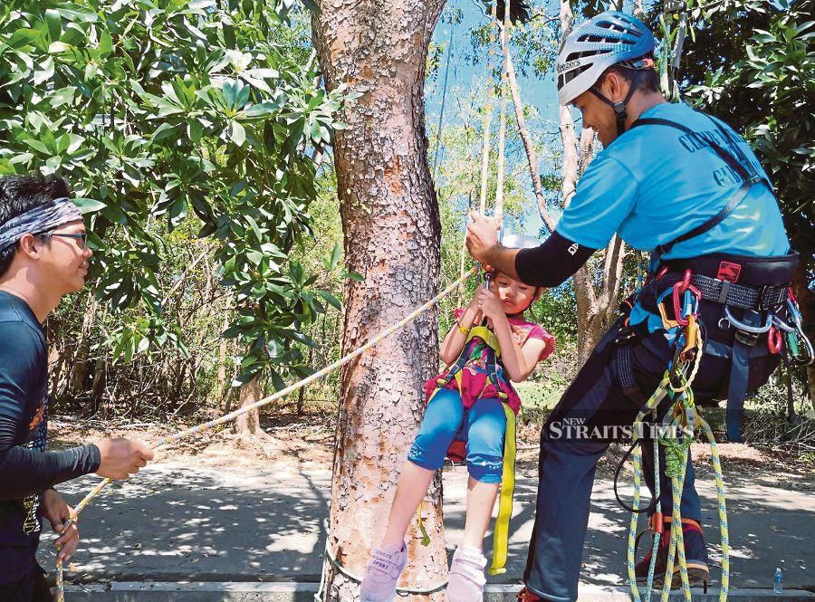 Unding Jami guiding a 6-year-old child to experience climbing a tree using single rope technique during Tree Climbing Awareness event at Sabah Indoor Climbing Centre in Likas near here. PIC BY OLIVIA MIWIL. 