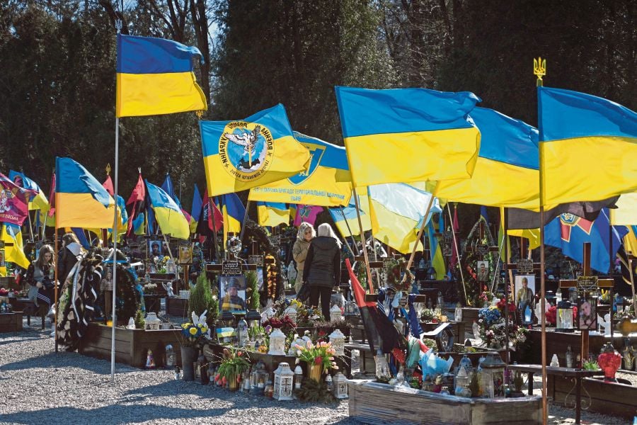  Visitors standing among graves decorated with the Ukrainian flag at the Lychakiv military cemetery in Lviv on March 18. AFP PIC 