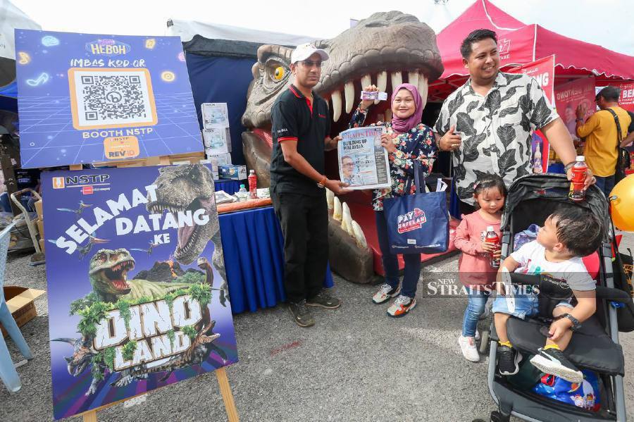 The General Manager of Distribution and Sales of The New Straits Times Press (NSTP) (M) Bhd, Prakash D Munusamy (left), gives newspapers and gifts to members of the public visiting the dinosaur tunnel or Dino Land at the NSTP booth during the Jom Heboh Carnival at the Batu Kawan State Stadium here. -NSTP/DANIAL SAAD