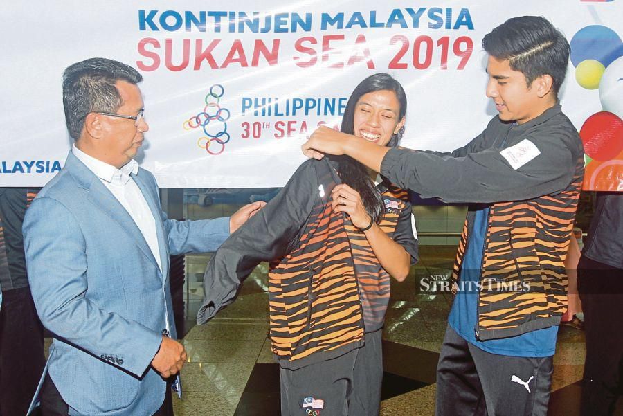 Sports Minister Syed Saddiq Syed Abdul Rahman (right) puts the national contingent jacket on Nicol David as OCM president Datuk Seri Mohamad Norza Zakaria looks on at KLIA yesterday. PIC BY MOHD FADLI HAMZAH