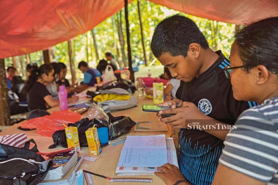   Kampung Kemidak Orang Asli students  from SRJK (C) Bekok using gadgets in online lessons under a canopy in a forest near Bekok recently.   PIC BY AIZUDDIN SAAD