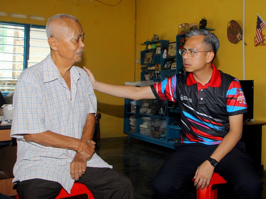 Communications and Digital Minister Fahmi Fadzil (right) presenting aid to Ng Kan Seng, at the latter’s home in Mambang Di Awan, Kampar. - BERNAMA PIC