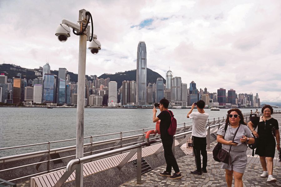 This photo taken on September 13, 2023 shows surveillance cameras (L) as people walk along the Kowloon side of Victoria Harbour in Hong Kong. (Photo by Peter PARKS / AFP)