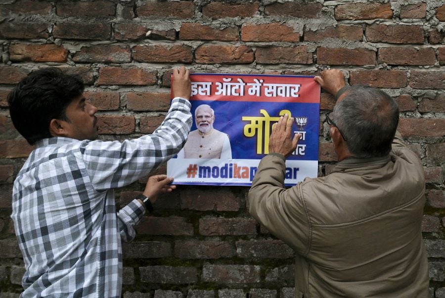 Bhartiya Janta Party (BJP) activists paste a poster with the image of BJP leader and Indian Prime Minister Narendra Modi on a wall near a polling station during the first phase of voting of India's general elections in Jammu. - AFP PIC