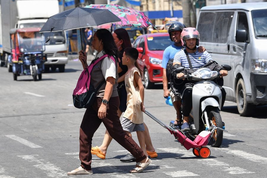  A family holding umbrellas to protect themselves from the sun walk across a street in Manila. - AFP PIC