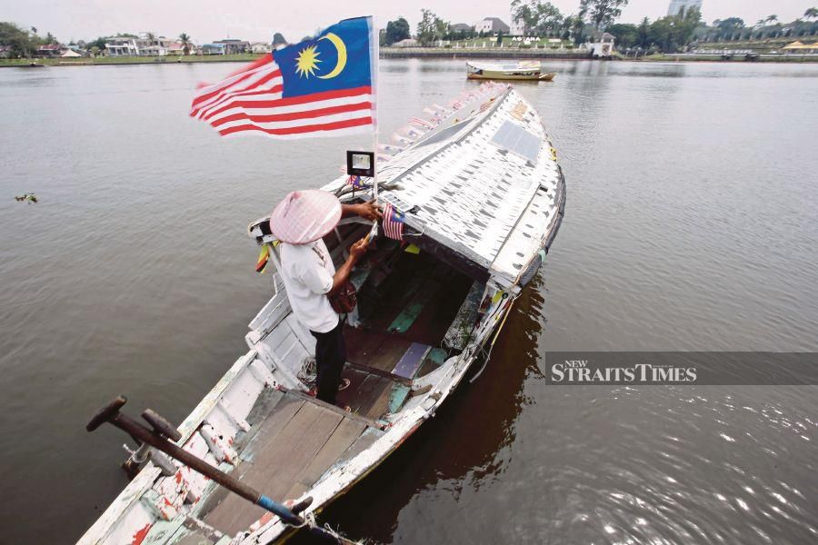 Boatman Ahmad Junaidi fixing a Jalur Gemilang to his boat before plying his trade across the Sarawak River in Kuching. PIC BY NADIM BOKHARI