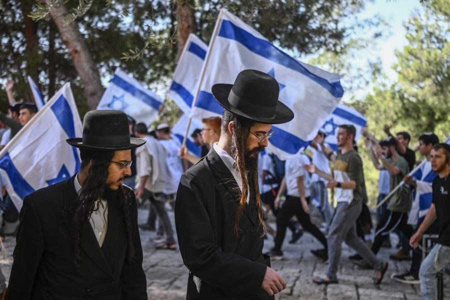 Two ultra Orthodox men walk past religious Israeli pre-military aged youth, wave their national flag as they protest outside the Old City of Jerusalem in support of Israel on October 26, 2023. - AFP Pic