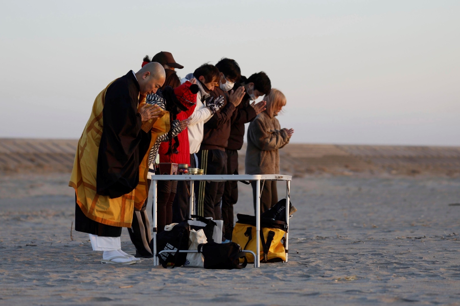 A monk and people offer prayers for the victims of the 2011 massive earthquake and tsunami, at a beach of Arahama district, Sendai city, Miyagi. - AP Pic