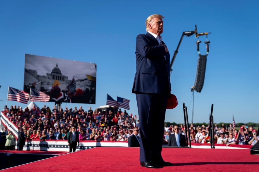 As footage from the Jan. 6, 2021, insurrection at the U.S. Capitol is displayed in the background, former President Donald Trump stands while a song, "Justice for All," is played during a campaign rally at Waco Regional Airport in Waco, Texas. - AP Pic