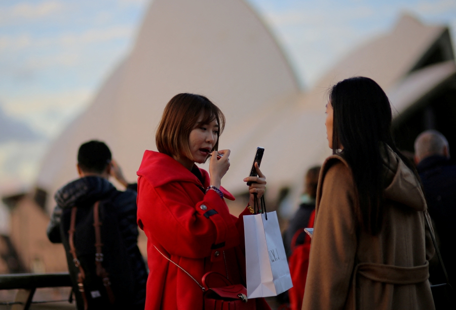 (FILE PHOTO) A tourist holding a shopping bag applies make-up before taking a picture in front of the Sydney Opera House in Circular Quay in Sydney, Australia. (REUTERS/Steven Saphore/File Photo)