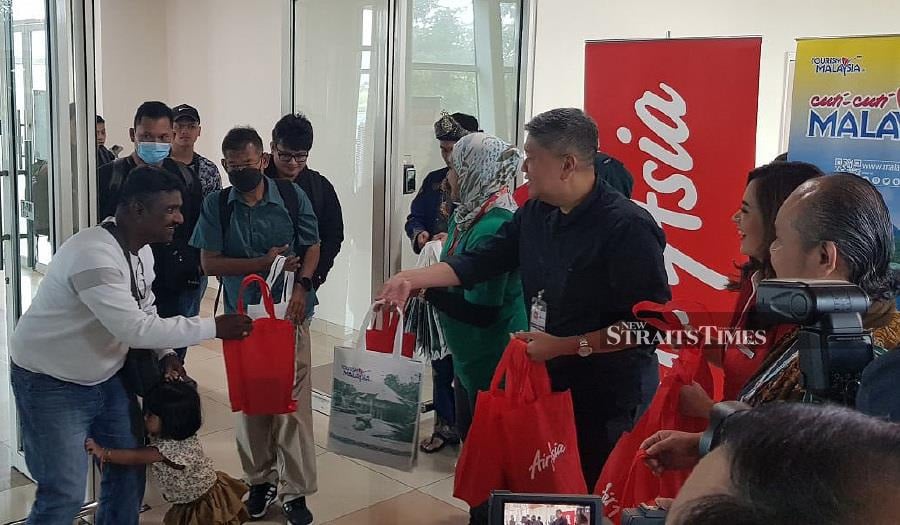 A young passenger on AirAsia’s first resumed direct flight from Penang to Kuching clings on to dad as Hamdan Mohamad, AirAsia head of Sarawak Affairs, presents goodie bags to arriving passengers. - NSTP/ BRUNO J