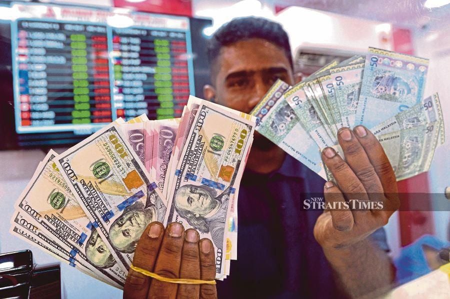 An employee at a moneychanger in Jalan Masjid India holds up ringgit and United States dollar notes. Bank Negara says the ringgit has been unfairly assessed against the dollar. NSTP file pic
