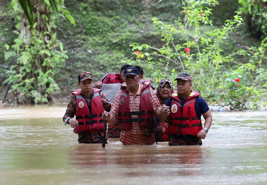Fire and Rescue Department personnel helping 75-year-old Dockery Raymond (centre) and his wife Rahilah, 68, (second, right) through floodwaters in Kampung Rancangan Cocos, Beluran. Bernama pic