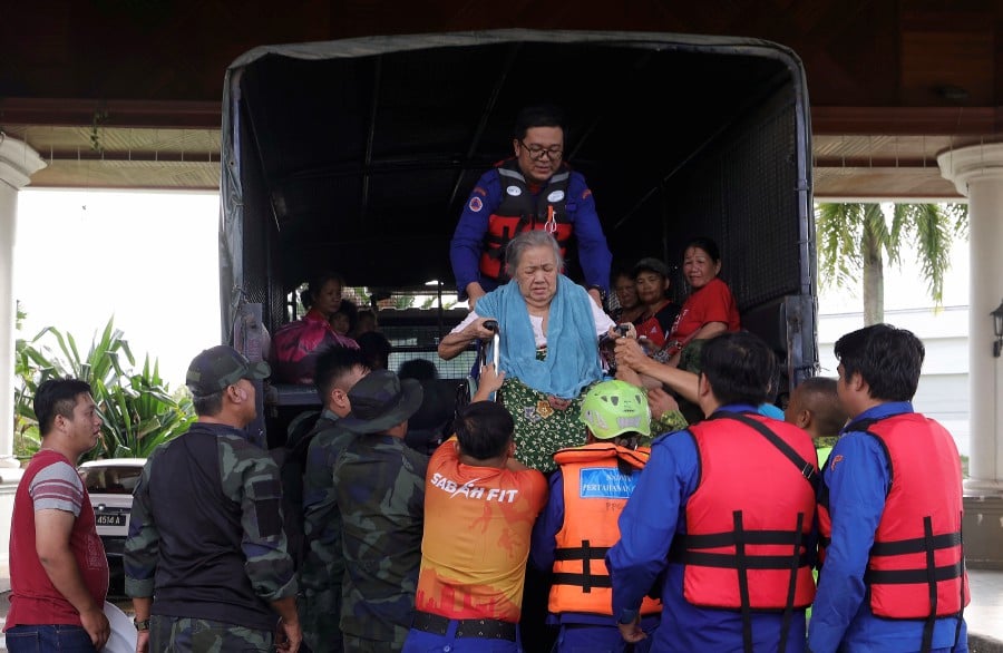 Justina Kodou, 82, of Kampung Toavon Penampang being helped by Civil Defence Force members from a vehicle after being moved to the temporary flood relief centre at the Penampang Cultural Centre. BERNAMA pic