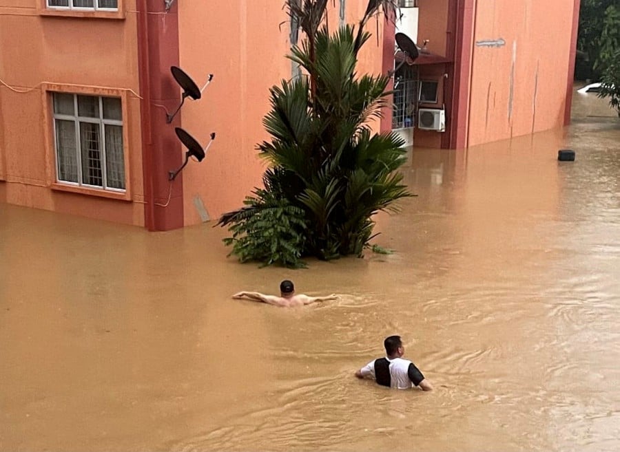 Vista Seri Kiranau residents wading through floodwater after heavy rain in the area today. -- BERNAMA PIC