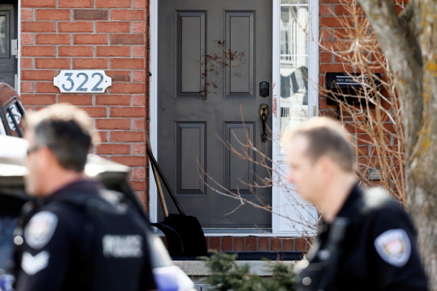 Ottawa Police Service officers walk past a door smeared in blood after four children and two adults were found dead inside a neighbouring house in the Ottawa suburb of Barrhaven, Ontario, Canada. -- REUTERS