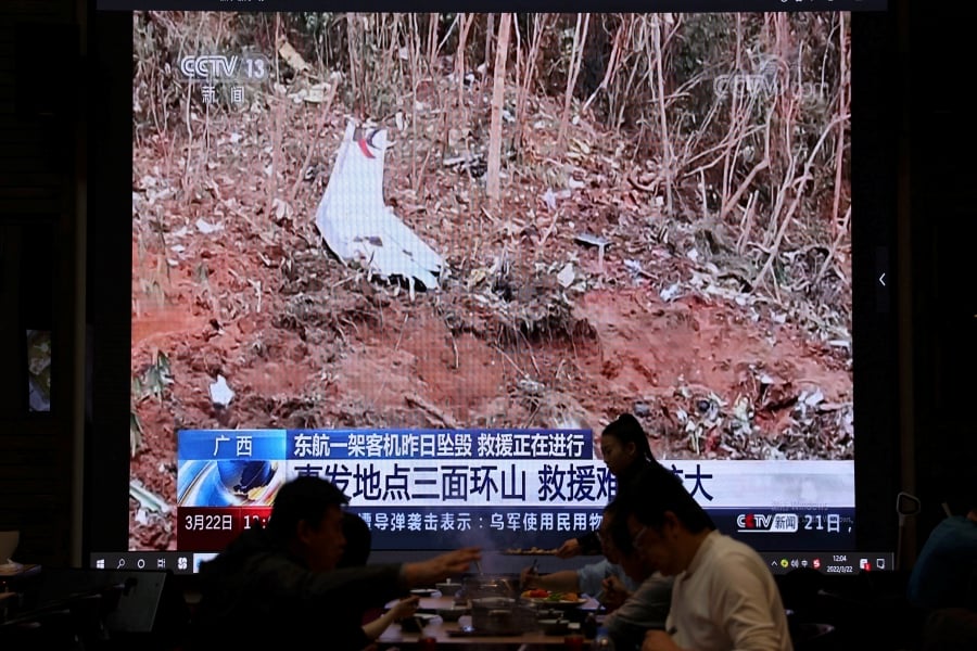A screen shows news footage of plane debris at the site where a China Eastern Airlines Boeing 737-800 plane flying from Kunming to Guangzhou crashed in Wuzhou of Guangxi Zhuang Autonomous Region, while customers dine at a restaurant in Beijing, China March 22, 2022. (Photo by REUTERS/Tingshu Wang)