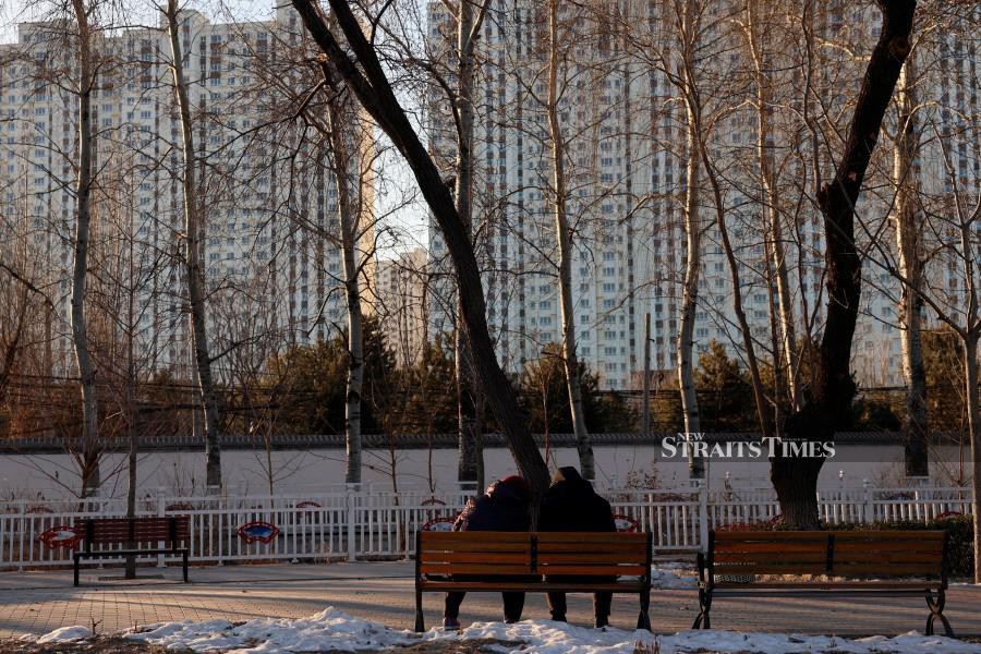 FILE PHOTO: People sit on a bench at a park near residential buildings in Beijing, China. REUTERS/Florence Lo/File Photo