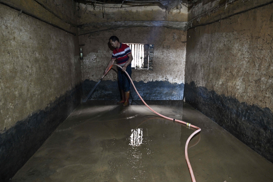 Lan Zhukui removes the mud left by floods from a warehouse where silkworms are stored in Sancuncun village, Yingde in China's Guangdong province. (Photo by Hector RETAMAL / AFP)