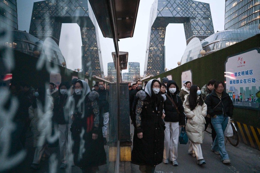 People walk on a sidewalk in the central business district in Beijing. (Photo by GREG BAKER / AFP)