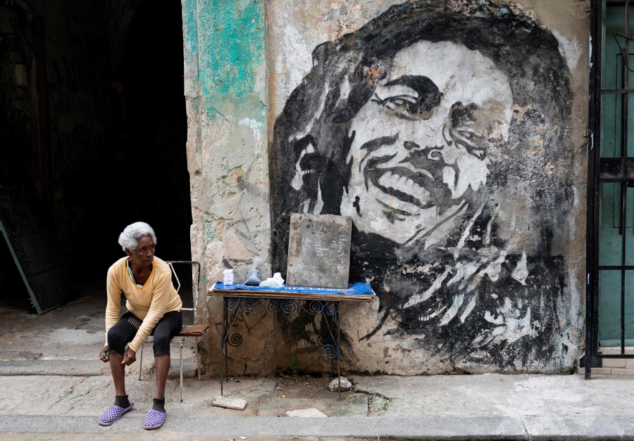 An elderly woman sells beans and cigarettes next to a mural depicting Jamaican singer Bob Marley in a street in Havana. (Photo by YAMIL LAGE / AFP)