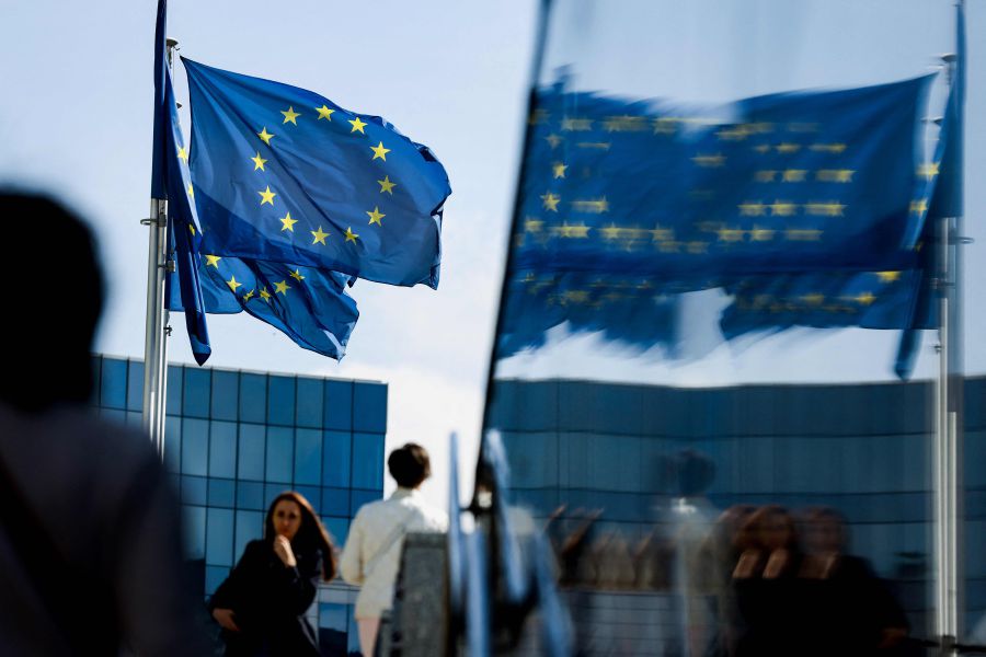People walk in front of the European Union flag in the area of the EU headquarters in Brussels. - AFP pic