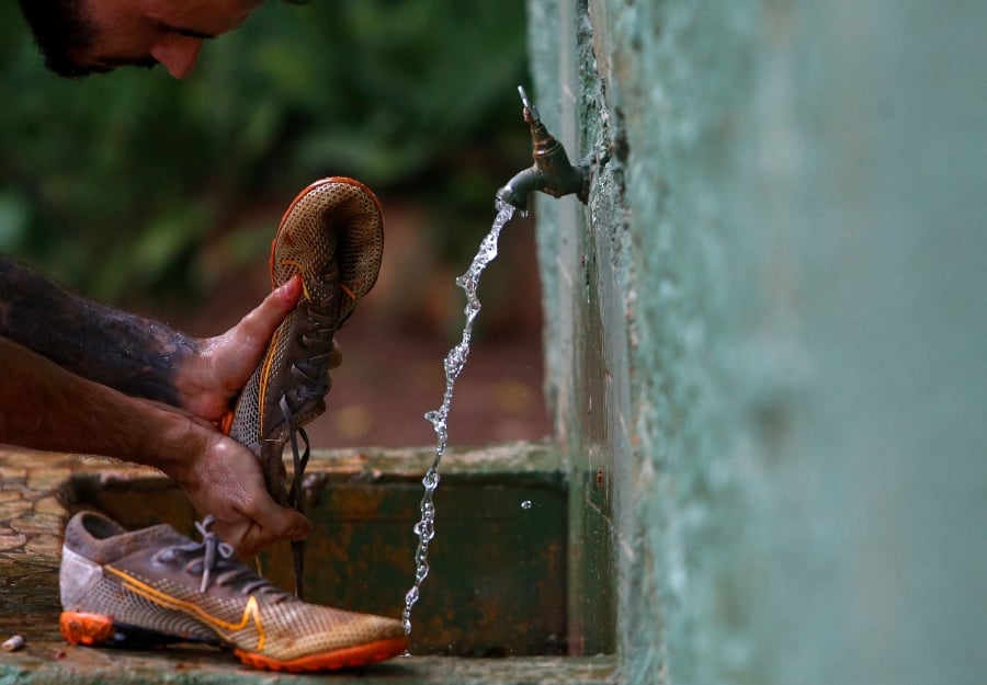 A man washes his football shoes after playing in a dirt field in Sao Paulo, Brazil. (Photo by Miguel SCHINCARIOL / AFP)