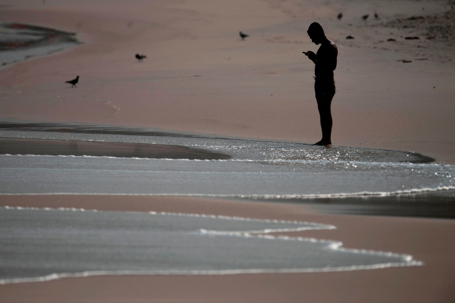 (FILES) In this file photo taken on June 2, 2020 a man uses a mobile phone at the Arpoador beach in Rio de Janeiro state, Brazil, during the novel coronavirus, COVID-19, pandemic. - (Photo by MAURO PIMENTEL / AFP) MAURO PIMENTEL