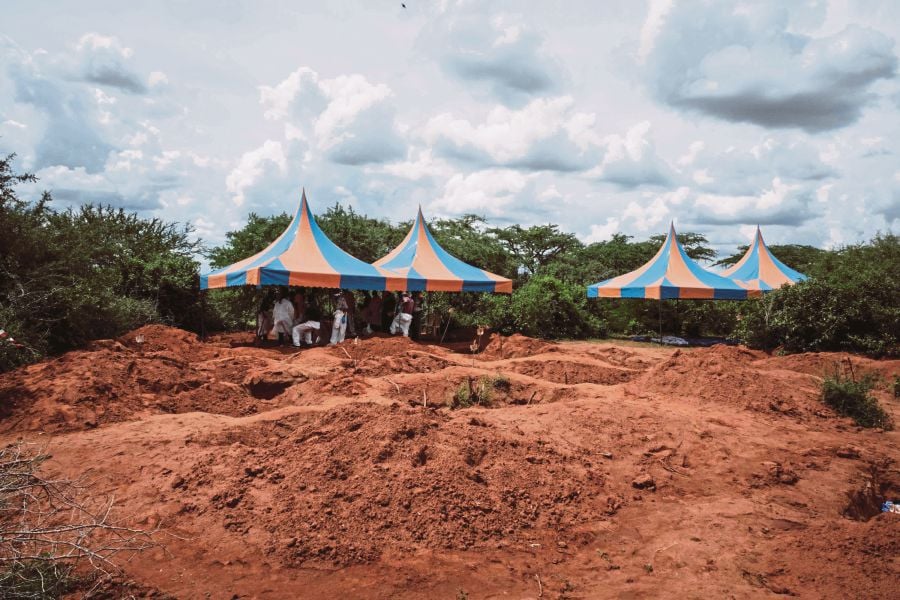 (FILES) Workers take shelter while digging the ground to exume bodies from the mass-grave site in Shakahola, outside the coastal town of Malindi. (Photo by Yasuyoshi Chiba / AFP)