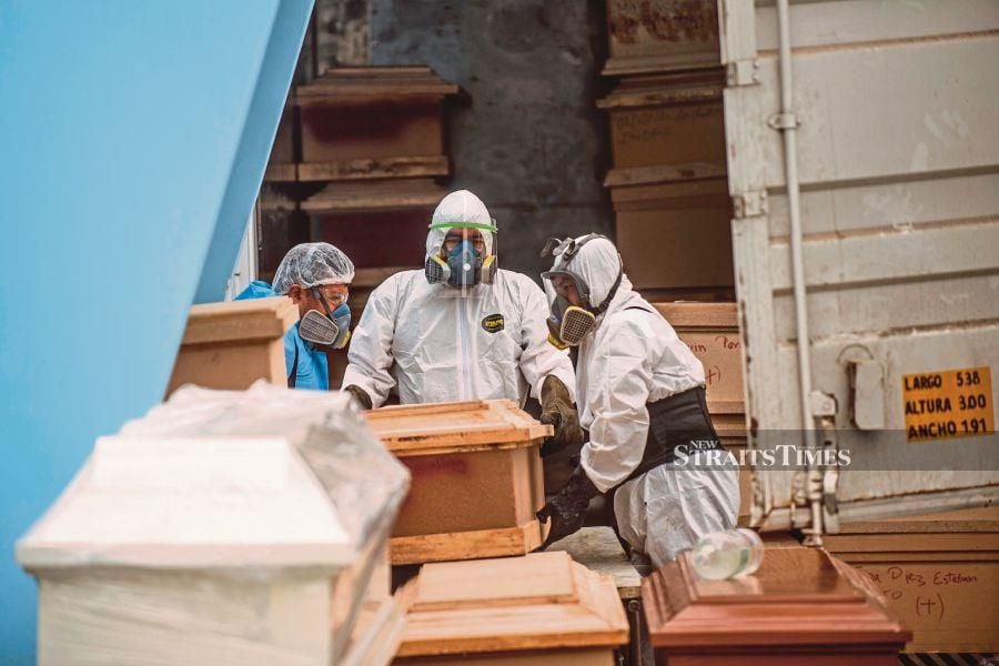 In this file photo taken on May 21 earlier this year, workers move a coffin with the body of a COVID-19 victim out of a refrigerated container before its cremation at the El Angel crematorium, in Lima. - (Photo by Ernesto BENAVIDES / AFP)