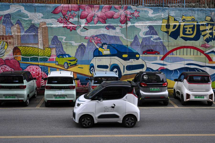 The photo taken shows a mini electric vehicle driving past a mural with electric cars on a street. (Photo by Jade GAO / AFP) 