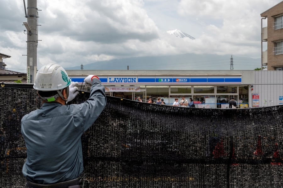 A worker installs a barrier to block the sight of Japan's Mount Fuji emerging from behind a convenience store to deter badly behaved tourists, in the town of Fujikawaguchiko, Yamanashi prefecture on May 21. — AFP