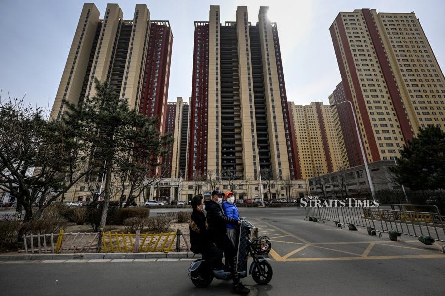 This photo shows people on a scooter riding past a residential compound. (Photo by Jade GAO / AFP)