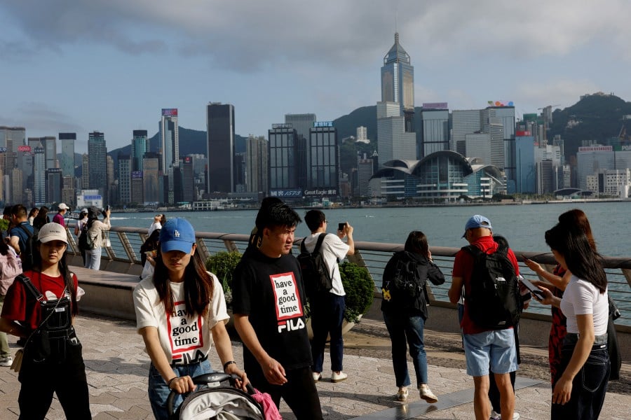 FILE PHOTO: Mainland Chinese tourists walk in front of the skyline of buildings at Tsim Sha Tsui, in Hong Kong, China May 2, 2023. REUTERS/Tyrone Siu/File Photo