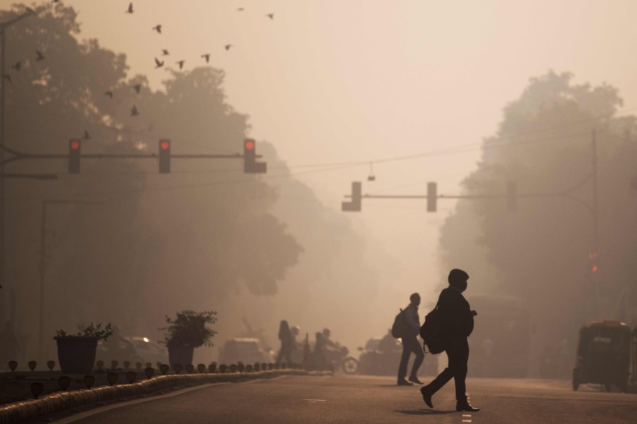 Commuters cross a street amid smoggy conditions in New Delhi. AFP FILE PIC