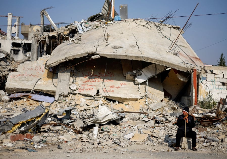 Ziad Mansour, a neighbour of the Abu Aweidah family, sits next to writing painted on a wall amid the rubble of the family's house, which was destroyed in a deadly Israeli strike amid the ongoing conflict between Israel and the Palestinian fighter group Hamas, in Rafah, Gaza Strip. (REUTERS/Mohammed Salem)