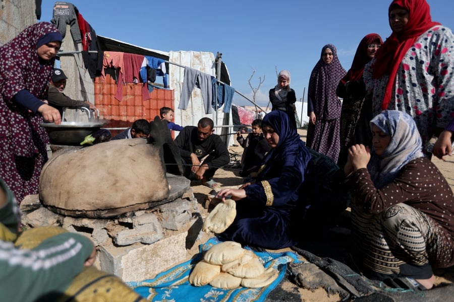 People wait while a woman prepares food, as displaced Palestinians, who fled their houses due to Israeli strike, shelter in a camp in Rafah, amid the ongoing conflict between Israel and Palestinian fighter group Hamas, in the southern Gaza Strip. (REUTERS/Ibraheem Abu Mustafa)